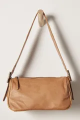 Bolso de hombro tipo baguette, color camel, confeccionado en cuero liso. Presenta un cierre superior y correa ajustable con hebillas metálicas plateadas.