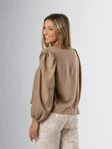 Blusa color beige con escote cuadrado y textura drapeada al frente. Sus mangas largas abullonadas aportan volumen y frescura.