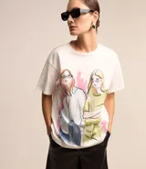 Remera de algodón color blanco con estampado de figuras femeninas de colores. Tiene cuello redondo y mangas cortas.