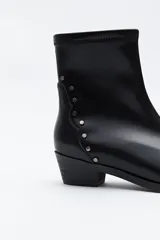 Bota corta de caña elástica, color negro, con puntera cuadrada y taco bajo. Presenta detalles de remaches metálicos plateados en el lateral exterior.