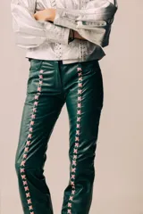 Pantalón de cuero de tiro medio y silueta recta levemente acampanada, color azul marino, con cierre frontal y recortes laterales intervenidos con pasacintas entrelazadas en contraste.