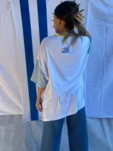 Remera de corte oversize confeccionada en tejido acanalado, con mangas cortas y cuello redondo. Presenta un parche bordado con la bandera de Uruguay en la parte superior de la espalda.