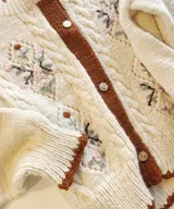 Cardigan de lana merino color marfil, con bordados florales artesanales, trenzas y rombos calados en el frente. Posee cierre frontal con botones vintage dorados y terminaciones en crochet celeste en cuello, puños, ruedo y tira de botones.
