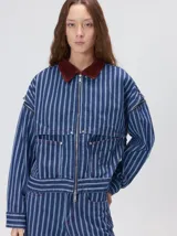 Campera de denim a rayas verticales con cuello de pana en color bordó. Presenta cierre frontal, mangas desmontables con cierre en los hombros, canesú en el pecho y bolsillos de parche cuadrados.