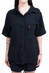 Camisa negra de manga corta con cuello clásico, bolsillo en el pecho y corte holgado.
