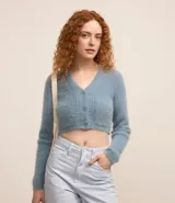 Cardigan cropped celeste de punto con pelitos, cuello en V, manga larga, cierre frontal con botones y bolsillos delanteros.
