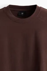 Remera H&M de algodón pesado, color marrón, con diseño boxy, cuello redondo ribeteado y mangas cortas con hombros caídos.