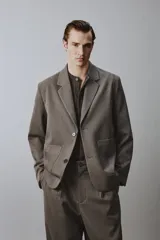 Blazer de corte relajado en color marrón oscuro, con cuello de solapas de muesca, cierre frontal de dos botones y bolsillos de plastrón en la parte delantera.