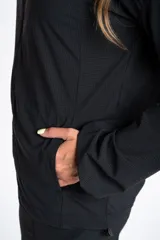 Campera deportiva de color negro con cierre frontal, capucha y mangas largas con puños elásticos. Presenta una textura ligera y un corte ajustado al cuerpo.