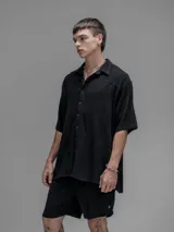 Camisa de corte oversize color negro, confeccionada en lino, con cuello tipo cubano, cierre frontal de botones y mangas cortas.