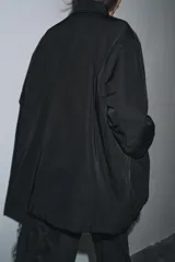 Chaqueta oversize de nylon en color negro, con cuello redondo subido, manga larga y cierre frontal con botones a presión ocultos. Presenta bolsillos delanteros y forro interior a tono.