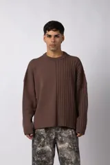 Sweater de punto color marrón con diseño asimétrico, presentando una mitad en tejido liso y la otra mitad con textura de trenzas verticales. Posee cuello redondo, corte holgado y mangas largas.