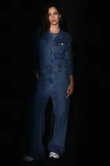 Mono de denim azul con cierre frontal de botones metálicos, cuello camisero, mangas largas y bolsillos delanteros.