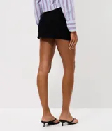 Short pollera mini de tiro bajo, confeccionado en bengalina negra. Presenta un diseño de cintura cruzada con detalle de hebilla ovalada metálica en el frente.