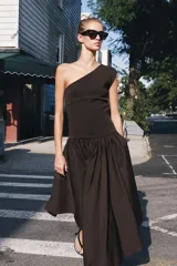 Vestido midi negro con escote asimétrico de un solo hombro, cuerpo ajustado y falda amplia de corte asimétrico con frunces en la cintura.