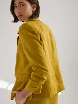 Blazer de lino color mostaza, inspirado en la sastrería clásica, con corte estructurado, solapas con pespuntes decorativos, cierre frontal con botones y bolsillos con tapa.