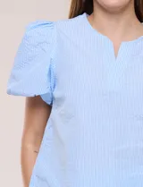 Blusa celeste a rayas blancas de calce recto con textura gofrada, cuello redondo con escote en V y mangas cortas abullonadas con elástico en los puños.