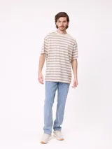 Remera de corte holgado con diseño de rayas horizontales en tonos beige, marrón y azul claro. Presenta cuello redondo, mangas cortas y un bolsillo frontal en el pecho con el logo de la marca bordado.