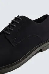 Zapato tipo derby con cordones, confeccionado en piel con acabado de serraje. Presenta horma redonda y suela a contraste.