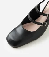 Zapato estilo Mary Jane de color negro, confeccionado en poliuretano con diseño cerrado y puntera cuadrada. Presenta tres tiras cruzadas en el empeine con hebillas metálicas ajustables, tira trasera con hebilla y taco bloque ancho.