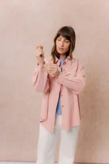 Camisa oversize de denim liviano color rosa, con cuello camisero, cierre frontal con botones, mangas largas con puños y dos bolsillos delanteros con tapa. Presenta un acabado desflecado en el ruedo.