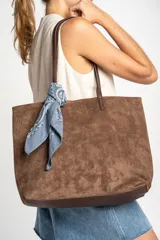 Bolso tipo tote grande de gamuza vegana color camel/marrón, con asas de cuero sintético marrón oscuro. Incluye un pañuelo bandana azul con estampado paisley atado a una de las asas.