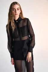 Camisa negra traslúcida de mangas largas con cuello clásico, cierre frontal con botones dorados y dos bolsillos frontales con solapa.