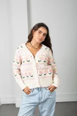 Cárdigan de punto color crema con diseño de flores en tonos rosados y verdes, guardas caladas, escote en V, cierre frontal con botones y terminaciones acanaladas.