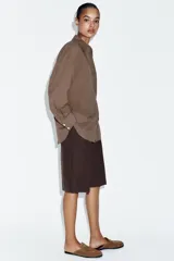 Camisa oversize de algodón con cuello solapa, manga larga y cierre frontal con botones. Presenta un bolsillo de plastrón en el frente y un diseño de corte amplio con ruedo redondeado.