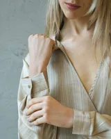 Conjunto de dos piezas en tono arena con textura plisada y acabado satinado. La parte superior es una blusa cruzada de manga larga con escote en V profundo y detalle de hebilla lateral. El pantalón es de corte wide leg con caída fluida.