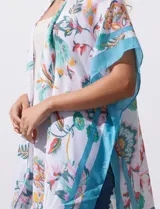 Kimono ligero de manga corta, color blanco, con estampado floral estilo cachemira en tonos pastel (naranja, verde menta, celeste). Presenta bordes y detalles en azul turquesa con borlas colgantes en el ruedo.