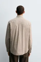Camisa de algodón de manga larga, cuello abotonado y cierre frontal de botonadura. Presenta un patrón de cuadros pequeños en tonos beige, marrón y blanco.