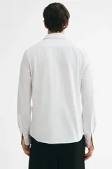 Camisa H&M de corte slim fit, color blanco, confeccionada en tejido elástico con cuello italiano y cierre frontal de botones.