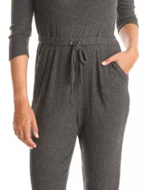 Enterito de tejido de punto con textura canalé, color gris oscuro. Presenta escote redondo, mangas tres cuartos y cintura elastizada con lazo de ajuste. La parte inferior tiene un calce relajado tipo jogger con puños elastizados y bolsillos laterales.