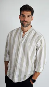 Camisa de manga larga con cuello mao y cierre frontal de botones. Presenta un diseño de rayas verticales en tonos beige y blanco, con un pequeño logo bordado en el pecho.