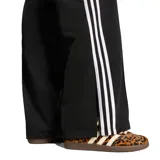 Pantalón deportivo Adidas de la línea Originals, confeccionado en tejido tricot de poliéster reciclado. Presenta un corte holgado con cintura media elástica, bolsillos laterales con cierre y el icónico diseño de las tres tiras blancas a lo largo de las piernas.