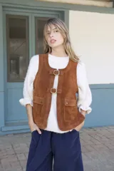 Chaleco de cuero gamuzado color marrón, con cierre frontal mediante dos hebillas metálicas y dos bolsillos frontales con solapa.