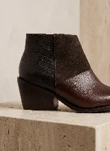 Bota corta de cuero vacuno en color marrón, con diseño de paneles combinados que incluyen textura de reptil en el talón, gamuza en el lateral y cuero liso en la puntera. Presenta un taco cuadrado de 6 cm y suela de caucho antideslizante.