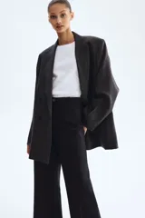 Pantalón negro de corte bootcut, con tiro alto, trabillas para cinturón y cierre frontal con botón y cremallera. Cuenta con pliegues marcados al frente y bolsillos simulados con solapa en la parte delantera.