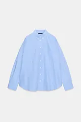 Camisa de corte oversize confeccionada en tejido de popelín con estampado de rayas verticales en azul y blanco. Presenta cuello camisero con botones, cierre frontal con botones, manga larga con puños y un bolsillo de plastrón en el pecho.