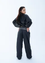 Pantalon deportivo de estilo urbano, confeccionado en tela técnica, con cintura elástica ajustable mediante cordón. Presenta un diseño bicolor en negro y gris oscuro con líneas laterales en contraste.