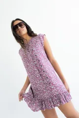 Vestido corto sin mangas en color rosado con estampado floral en blanco y negro. Presenta una cartera de botones asimétrica en el frente y detalle de volado fruncido en el ruedo. Confeccionado en algodón liviano.
