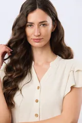 Camisa de lino y viscosa color beige, con cuello mao, escote en V y botones frontales de madera. Presenta mangas cortas con volados delicados.