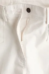 Pantalón de sarga color blanco de corte acampanado y tiro alto, con bolsillos delanteros de parche con solapa y botones oscuros, y pliegues marcados en el centro de las piernas.