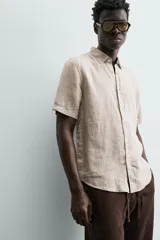 Camisa de lino color beige de corte relajado, con cuello solapa, manga corta y cierre frontal con botones.