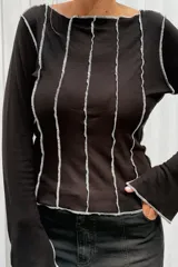 Remera de manga larga color negro, con cuello redondo y diseño de costuras verticales expuestas en color blanco que recorren el frente y las mangas.