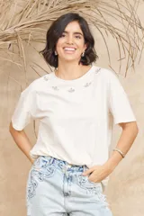 Remera color crema de algodón suave, de manga corta y cuello redondo. Presenta apliques de strass en el escote.