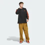 Camisa polo Adidas de manga larga en color negro, con cuello clásico y las icónicas tres tiras naranjas en las mangas. Presenta el logotipo del trébol bordado en naranja en el pecho con la inscripción 'Basketball'.