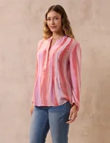 Blusa de gasa estampada con flores en tonos rosa, amarillo y azul. Tiene cuello a la base, escote en V y botones. La delantera tiene detalle plisado y las mangas son 3/4 regulables con presilla y botón.