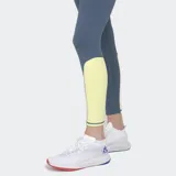 Calza deportiva de tiro alto, color gris azulado, con recortes laterales en amarillo claro. Presenta paneles con microperforaciones en la zona de la cadera y una franja vertical amarilla en la parte inferior de las piernas.